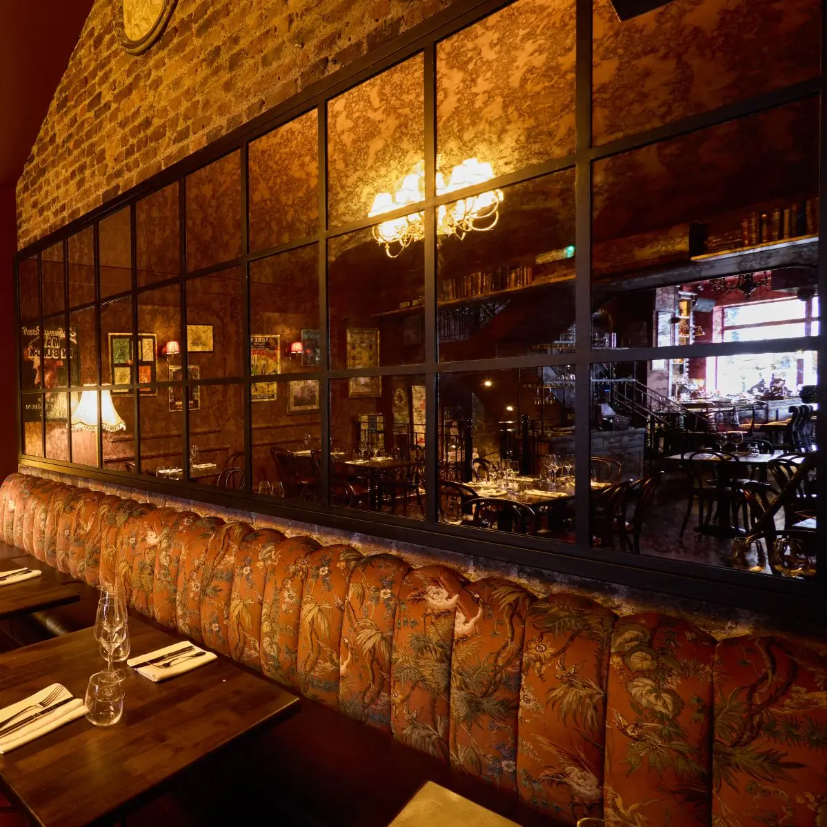 The warm interior of Fitzers Bistro, showing a plush, patterned banquette seat against an exposed brick wall and a large feature mirror reflecting the cozy dining room.