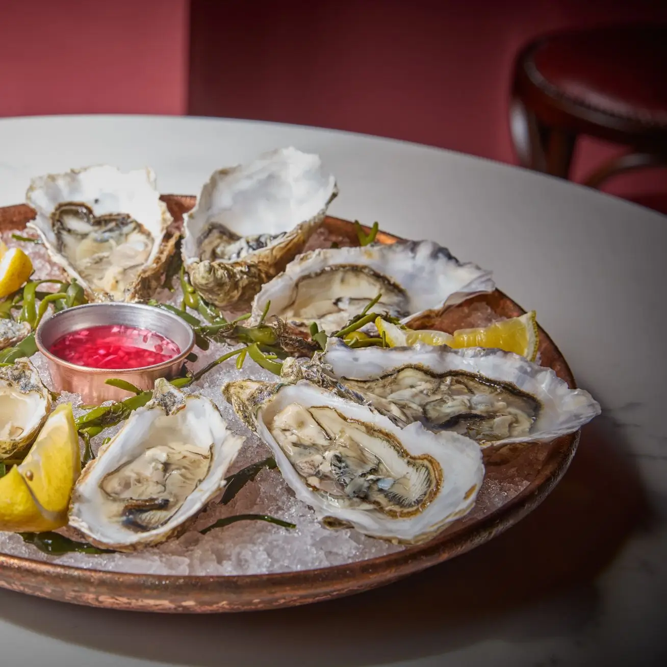 A copper platter of freshly shucked Irish oysters on a bed of crushed ice, served with lemon wedges and a vibrant mignonette sauce.