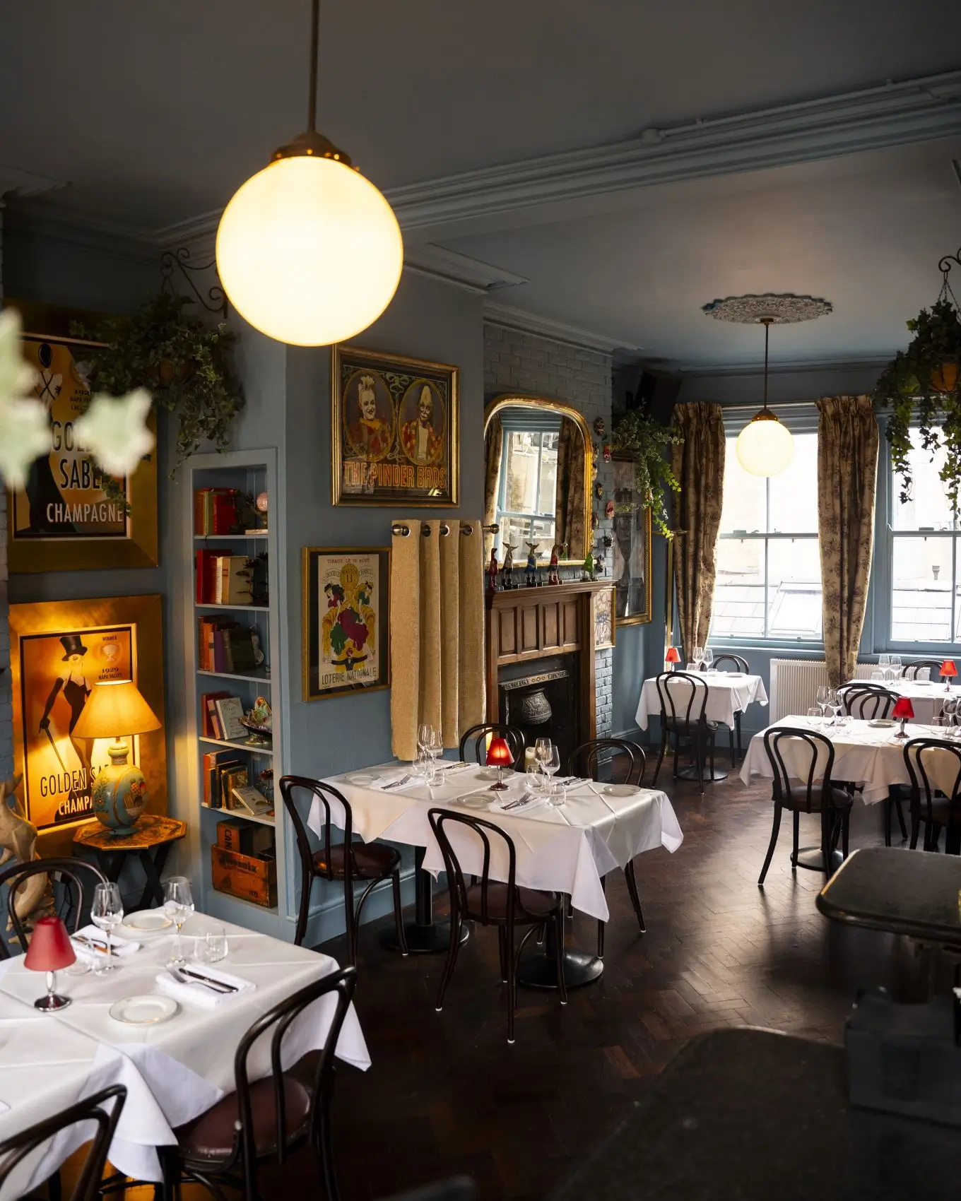 The elegant interior of the Blue Room at Fitzers Bistro, set for private dining with white tablecloths, dark wood chairs, and eclectic art on blue-grey walls.