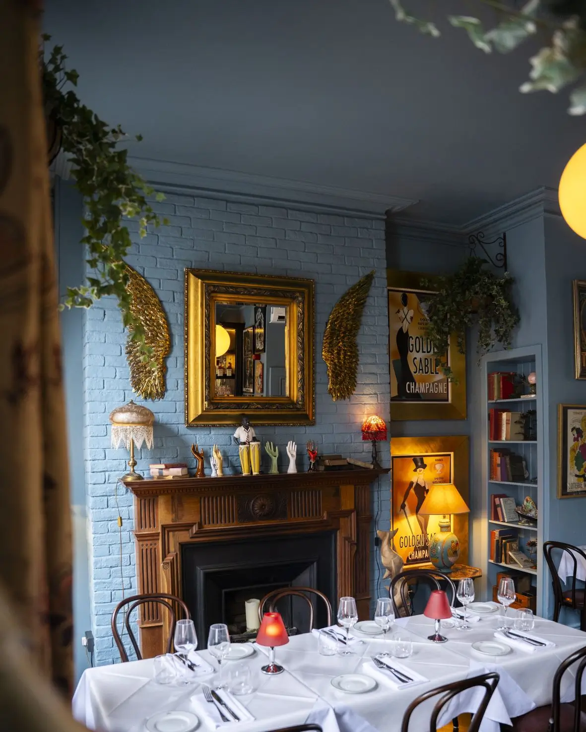An angled view of the Blue Room at Fitzers Bistro, focusing on the feature fireplace with golden wings, eclectic art, and a set dining table.