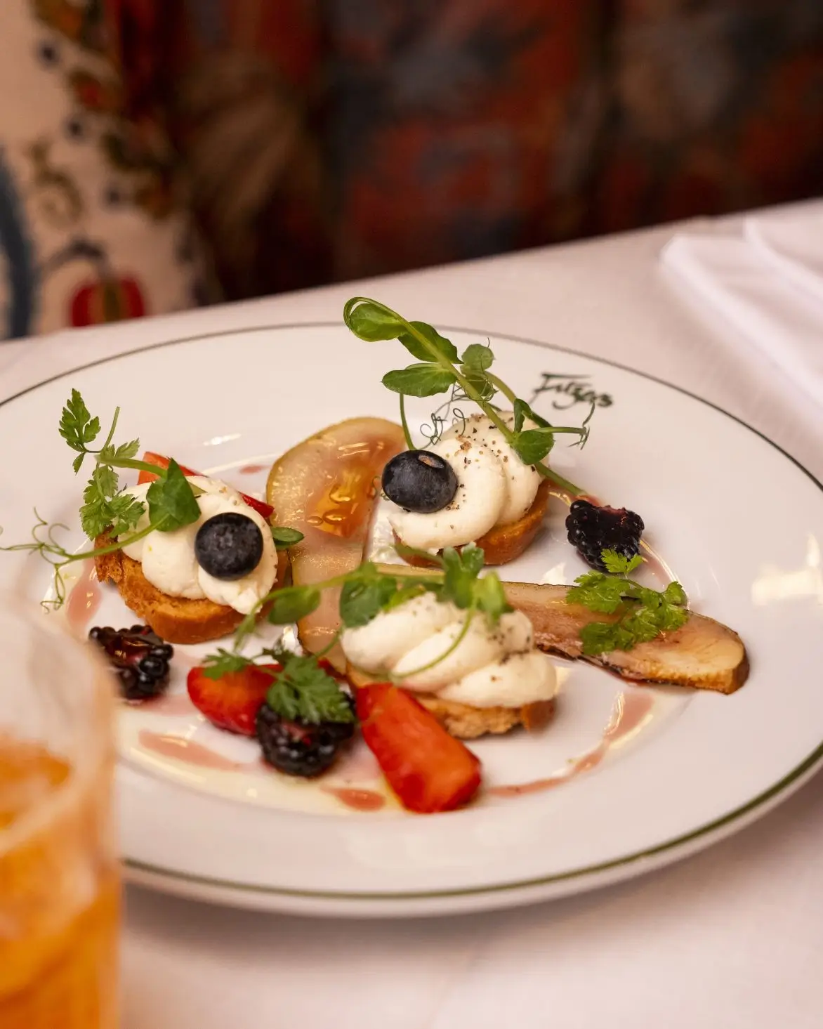 A close-up of Fitzers' Whipped Dublin Hills Goats Cheese Crostini, elegantly plated with fresh autumn berries, sliced pear, and a red wine agro dolce drizzle.